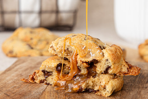 Caramel being drizzled over a chocolate chip cookie on a wooden board.